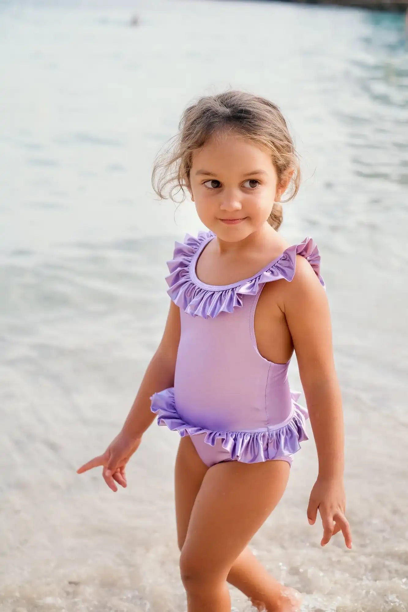 Girl in lilac ruffle swimsuit by Lison Paris at the beach, UV protection swimwear