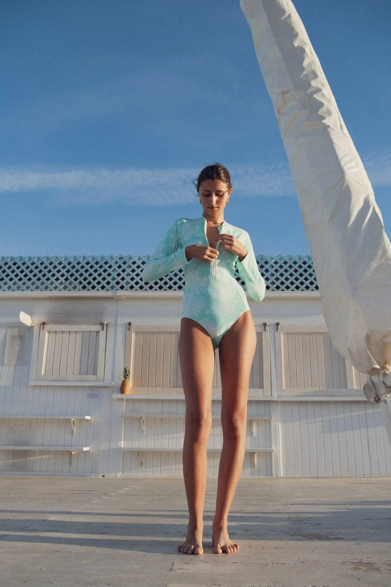 Girl wearing long sleeve aqua tie-dye UV-protective swimsuit outdoors under blue sky