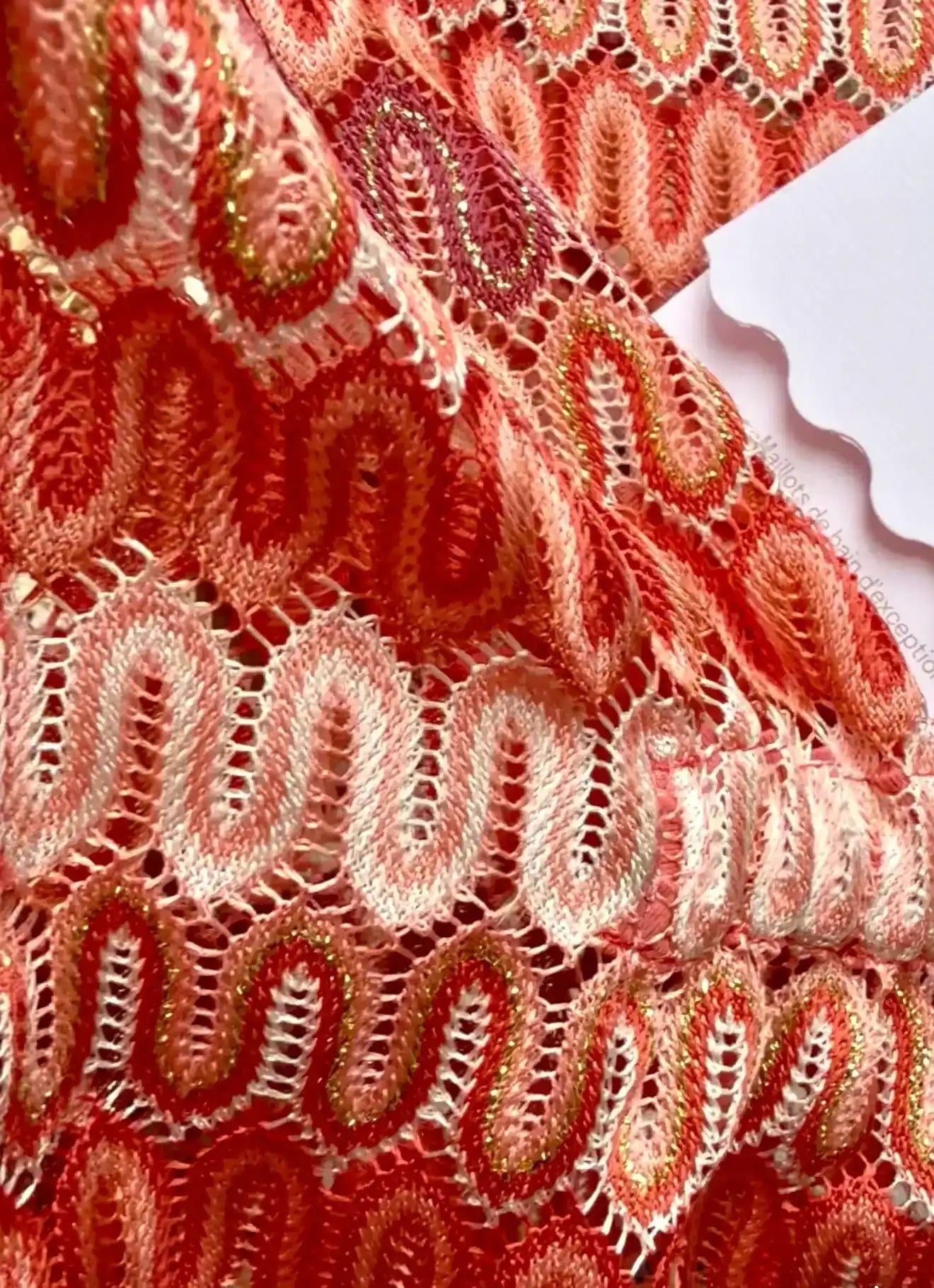Close-up of coral crochet one-piece swimsuit fabric with wavy patterns, Lison Paris beachwear.