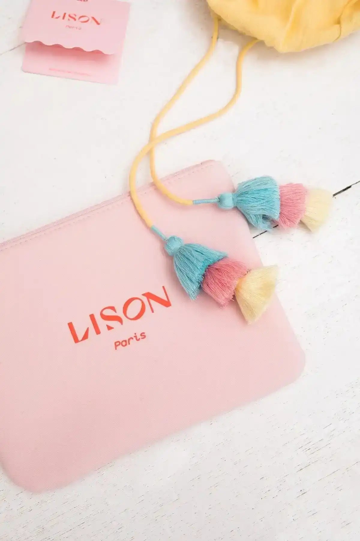Pink pouch with colorful tassels and yellow drawstring on a white surface