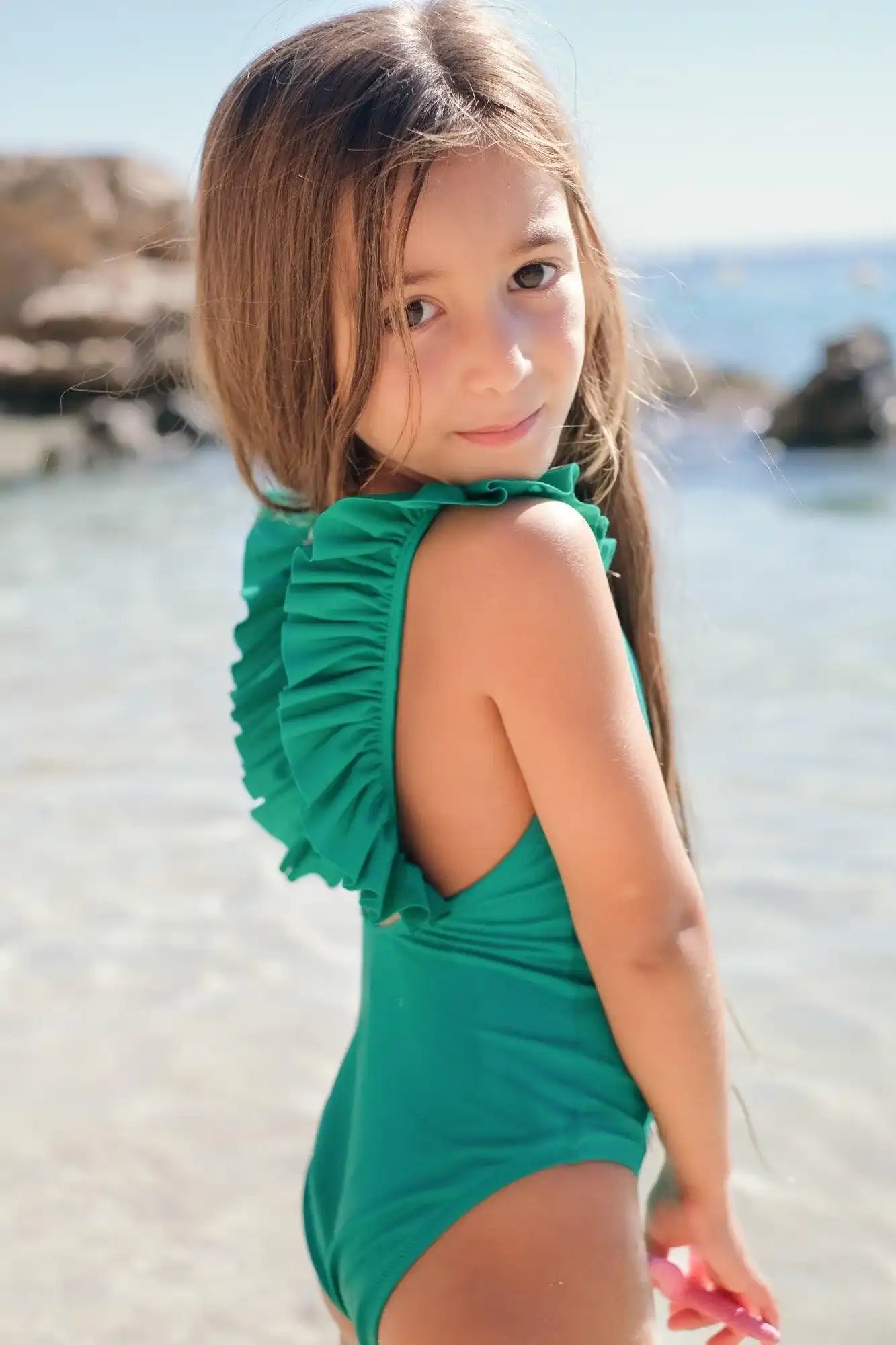 Girl in green ruffled one-piece swimsuit by Lison Paris on the beach