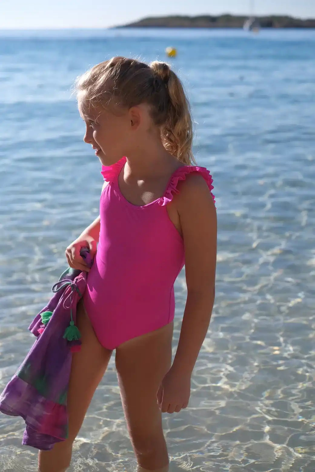 Girl in fuchsia one-piece ruffled anti-UV swimsuit by Lison Paris on the beach