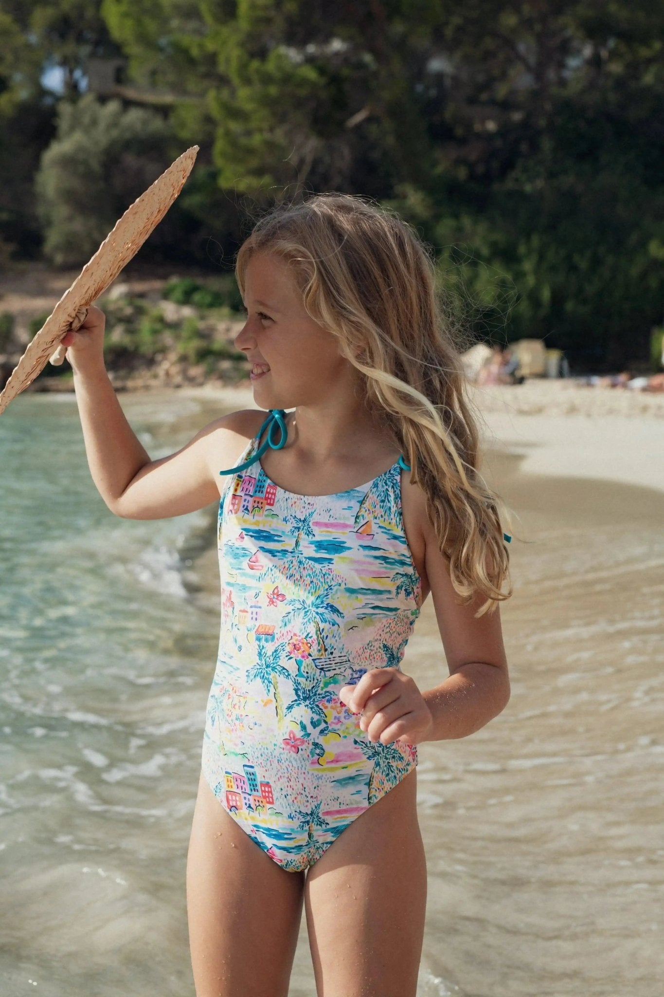Girl in colorful one-piece swimsuit with tropical print standing on a sandy beach
