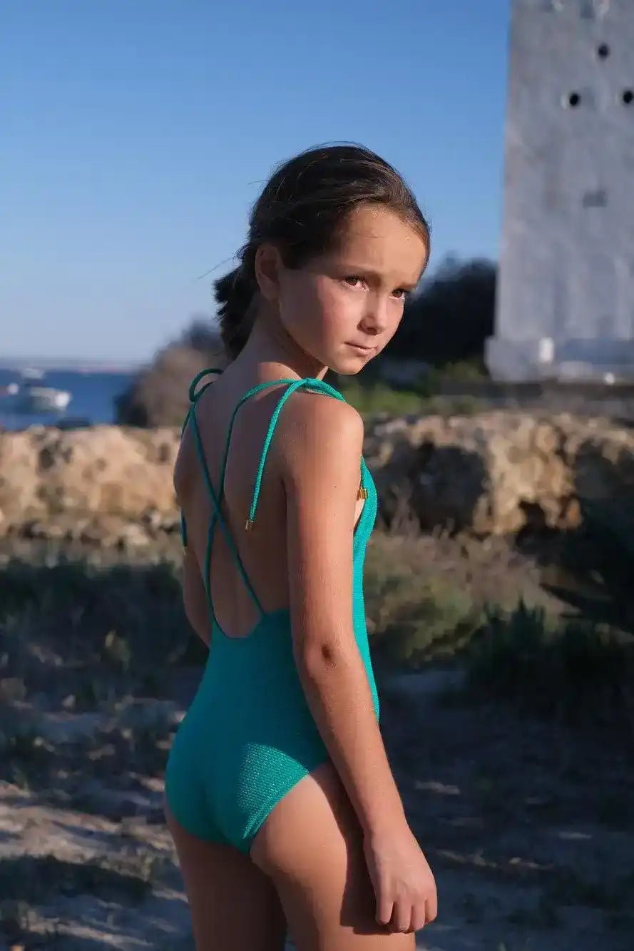 girl in green textured one-piece swimsuit with crisscross straps outdoors, summer beachwear