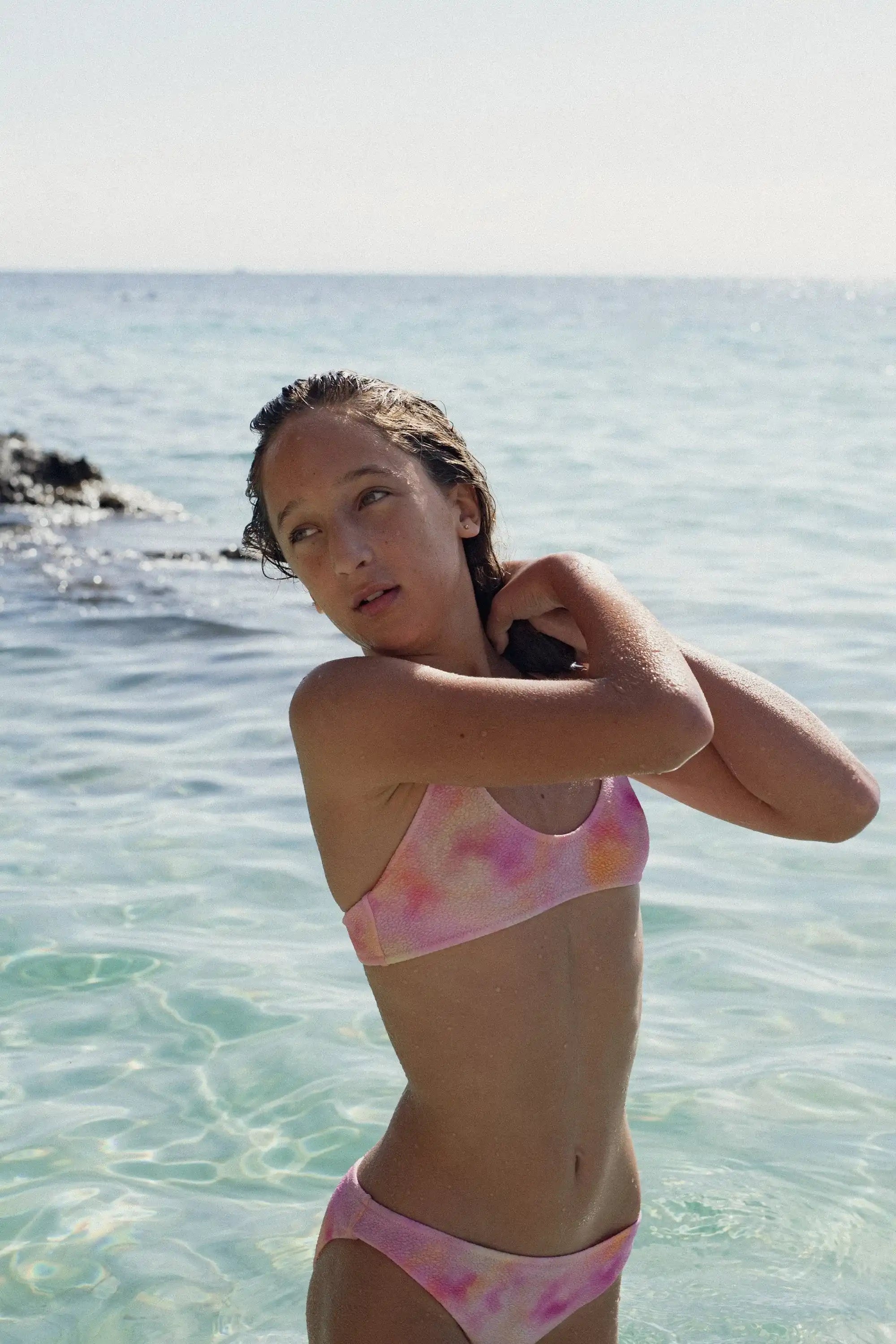 Girl wearing Lison Paris pink printed two-piece swimsuit in clear blue sea