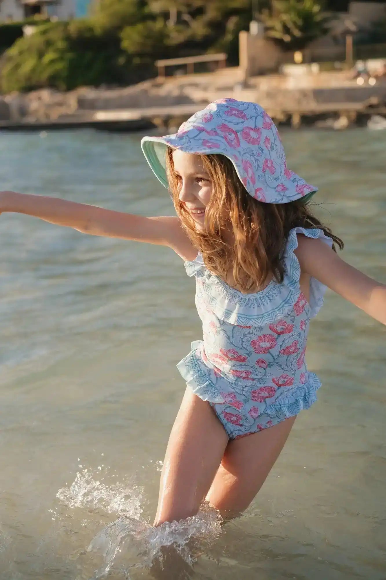 Girl playing in water wearing a ruffled floral one-piece swimsuit and sun hat