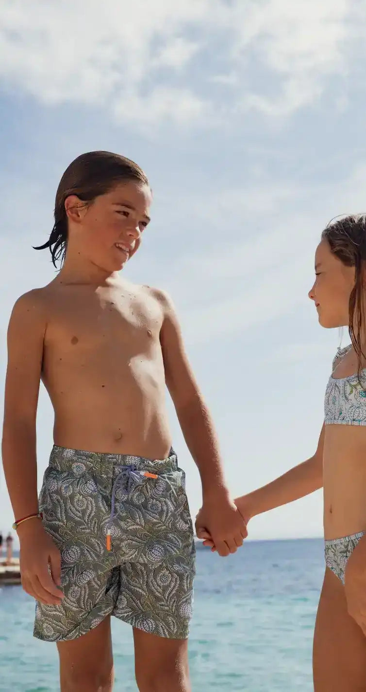Boy in printed green swim shorts and girl in bikini holding hands on the beach