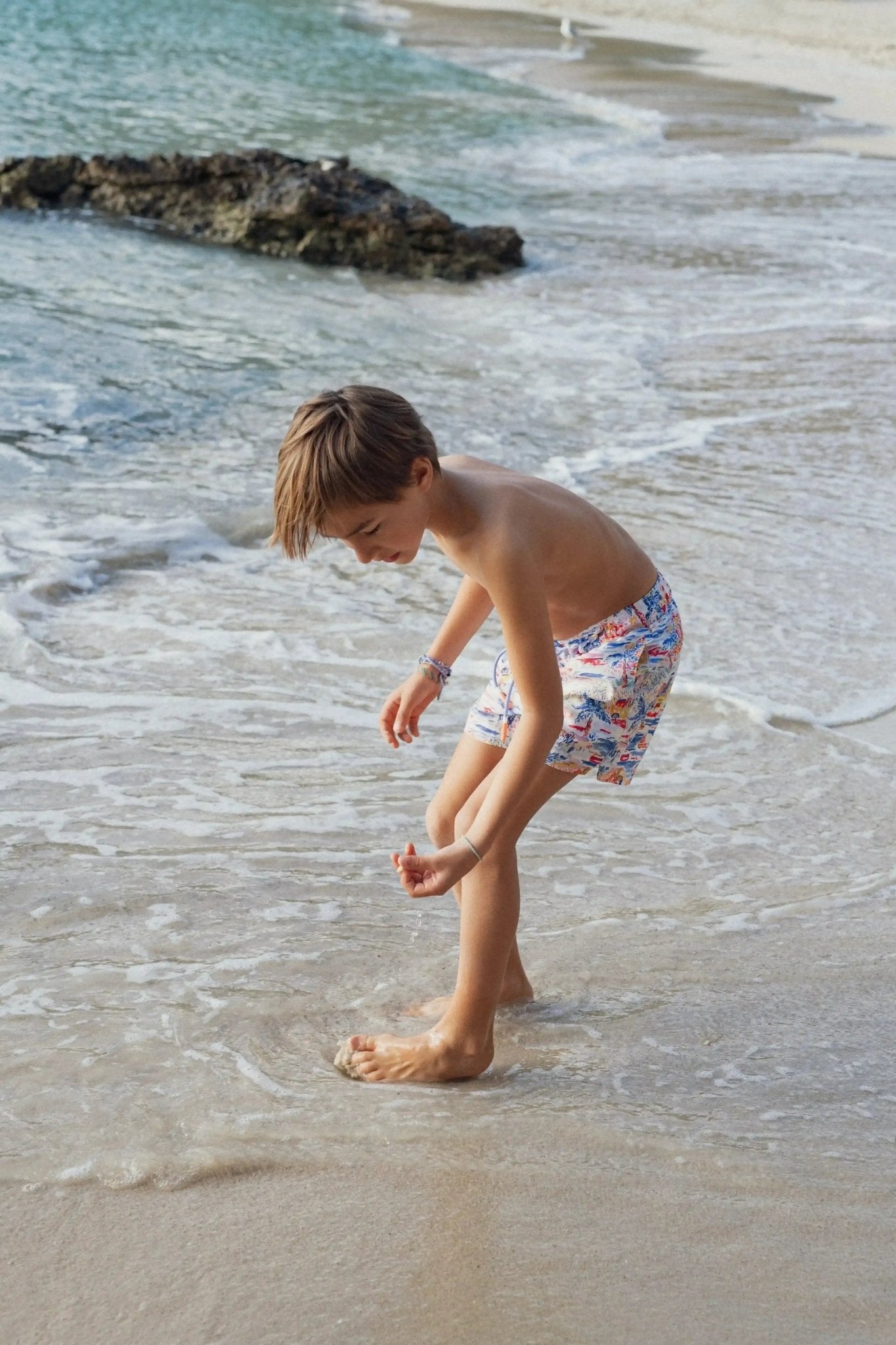 Boy in printed swim shorts playing at the beach near the shoreline