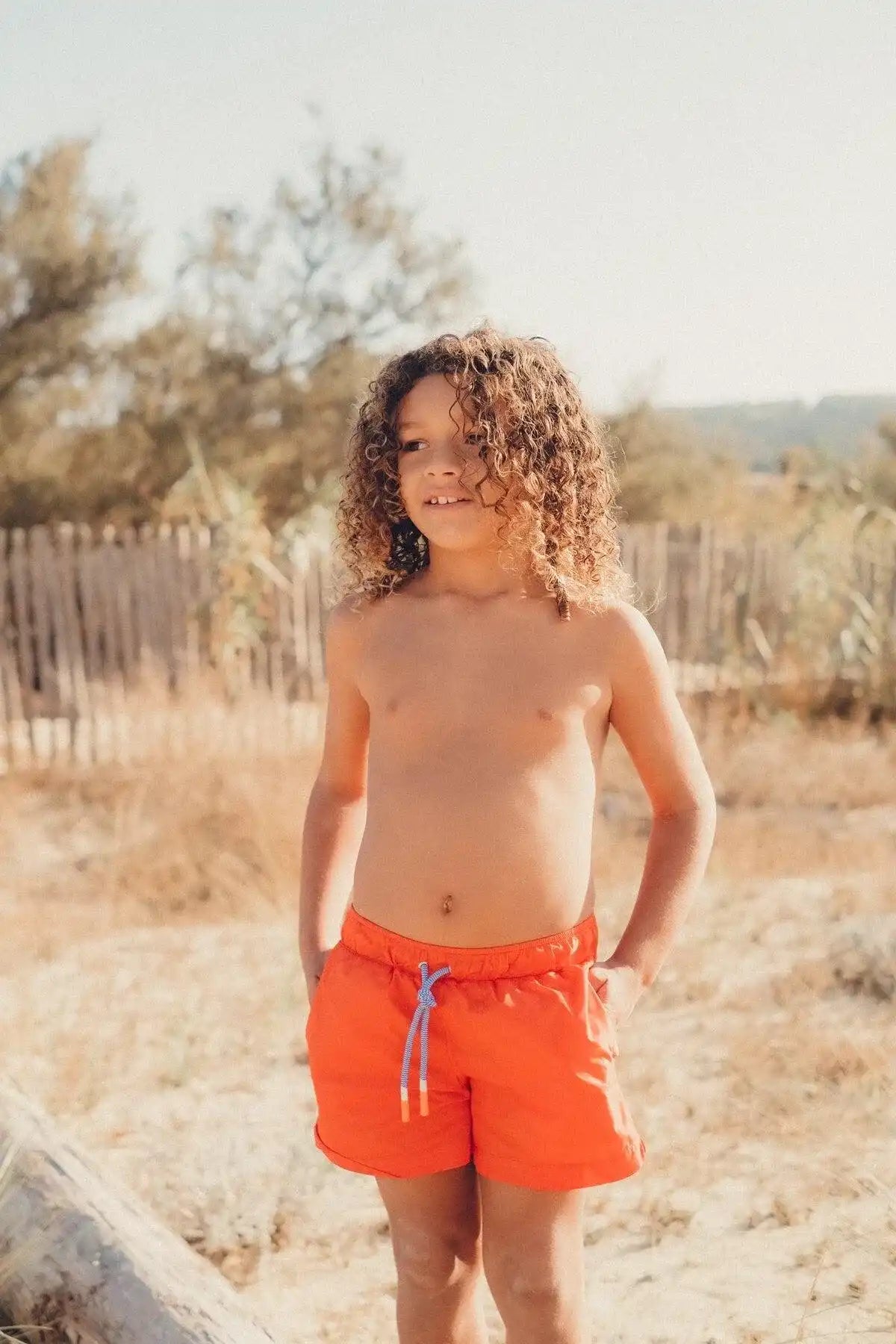 Boy wearing orange swim shorts outdoors, Lison Paris UV-protective kids beachwear collection