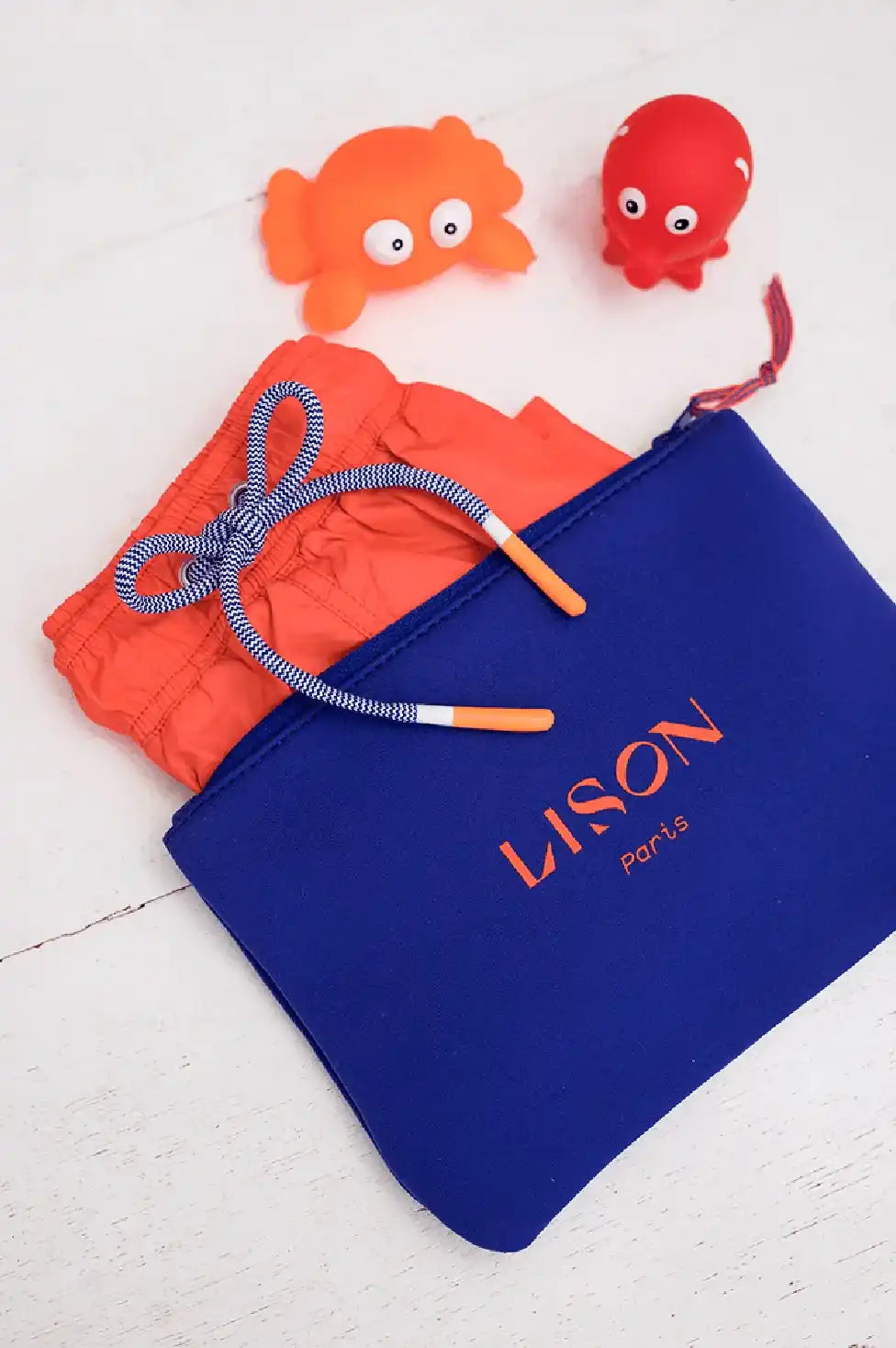 Orange boys' swim shorts with blue drawstring, Lison Paris pouch, and toy sea animals.