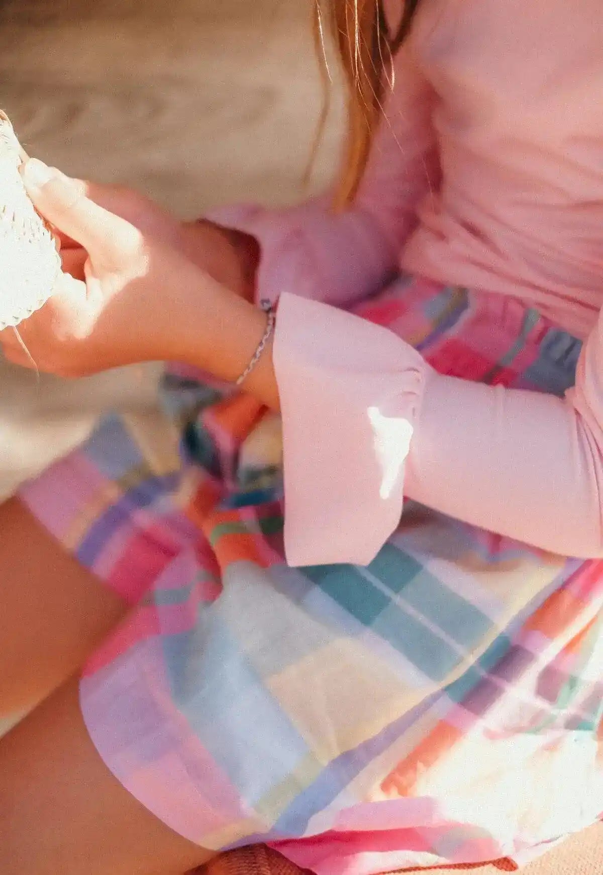 Girl wearing a pale pink long-sleeve UPF 50 shirt and colorful plaid skirt in sunlight