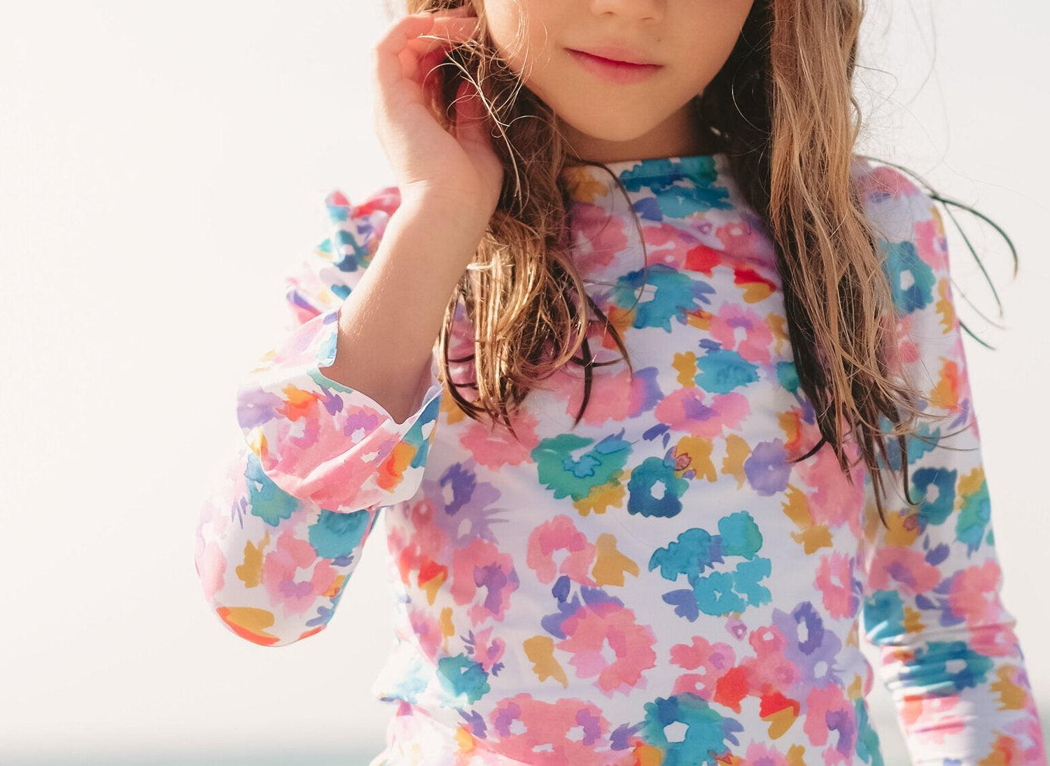 Girl in long-sleeve UV swim shirt with colorful floral print at the beach