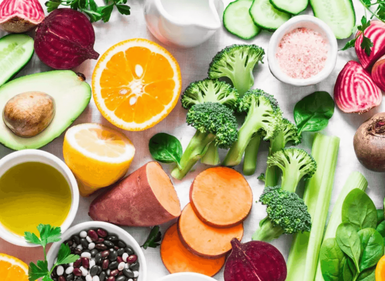 Fresh fruits and vegetables including oranges, avocado, sweet potato, broccoli, and beans.