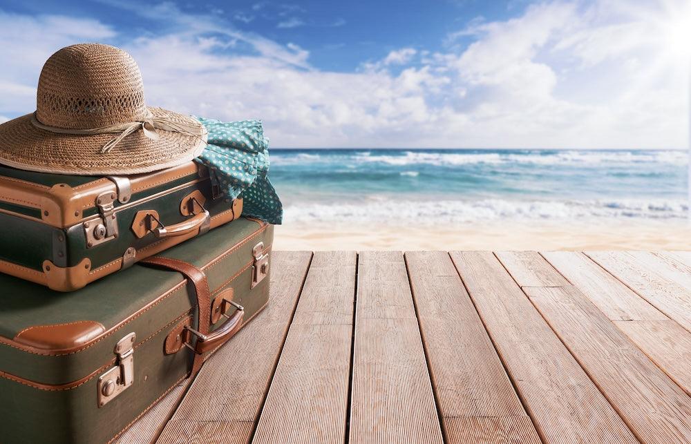 Suitcases and sun hat on wooden deck by the beach with ocean and sky in the background