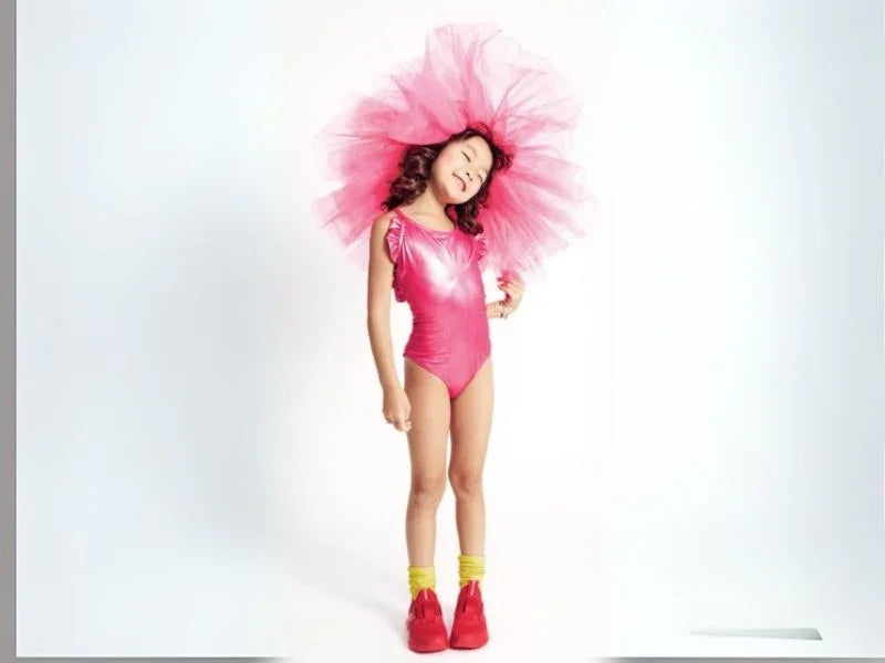 Girl wearing metallic pink one-piece swimsuit, pink tulle headpiece, yellow socks, red shoes