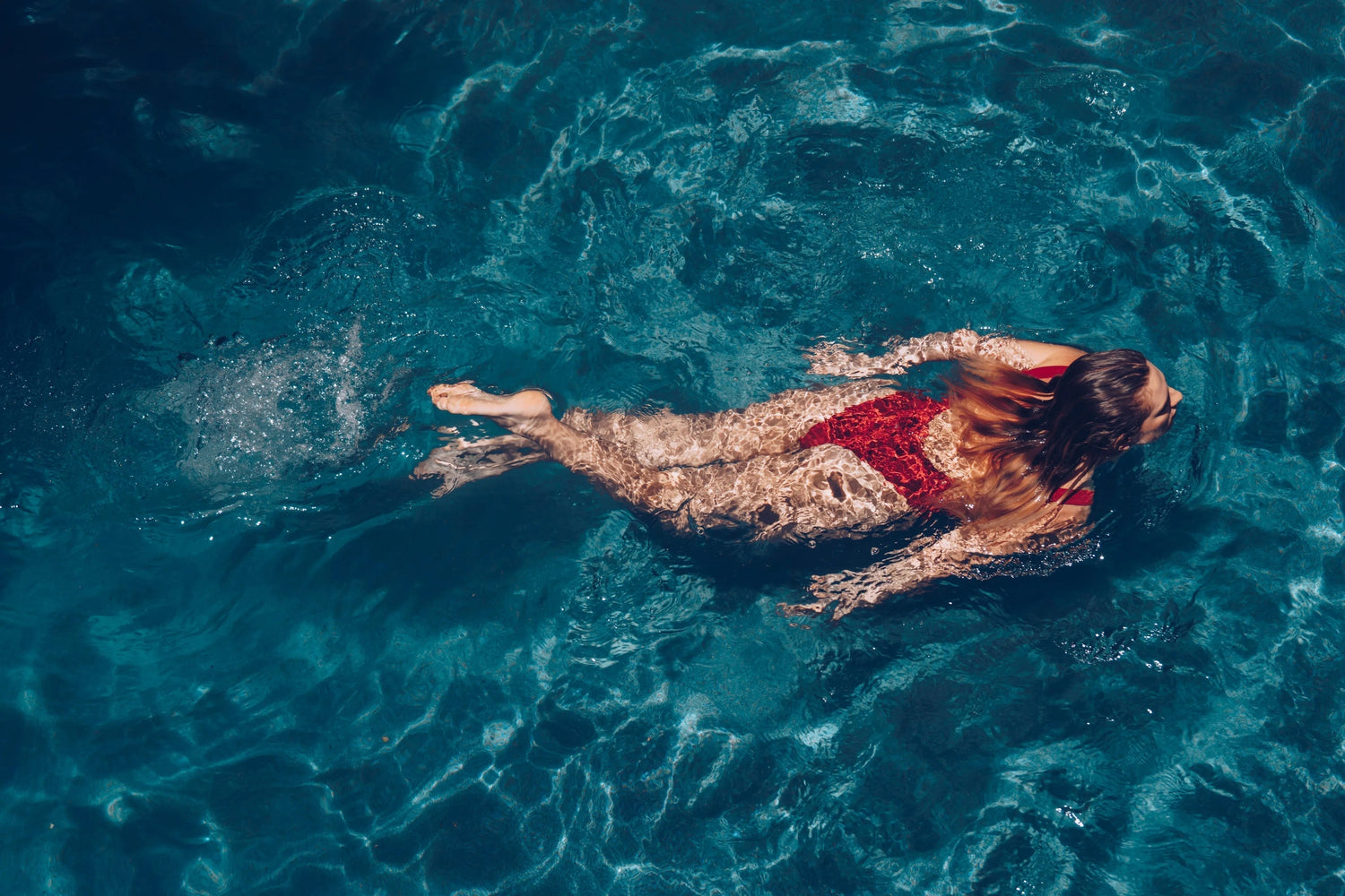 Woman swimming in clear blue water wearing a red swimsuit