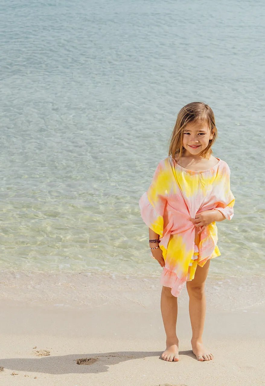 Young girl in a yellow and pink tie-dye caftan standing on a sandy beach