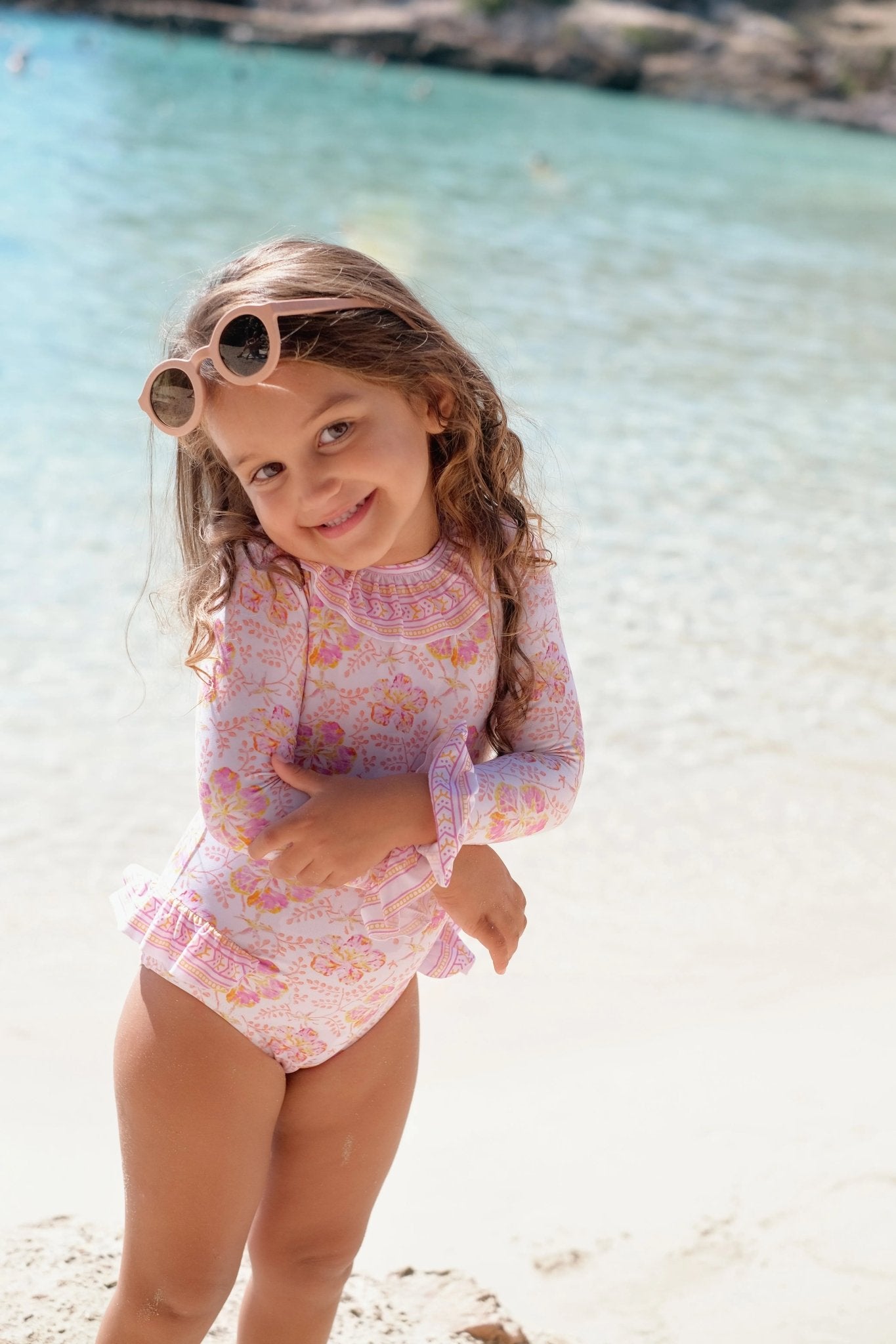 Smiling girl in floral long-sleeve swimsuit and sunglasses on a sunny beach