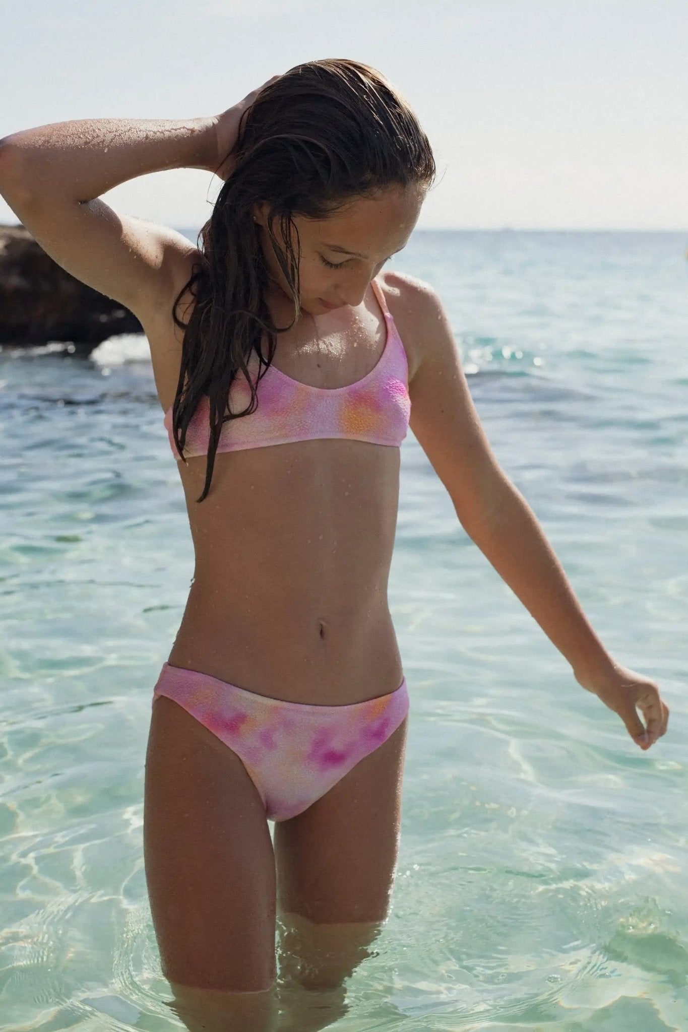 Girl in colorful two-piece swimsuit standing in clear water at the beach