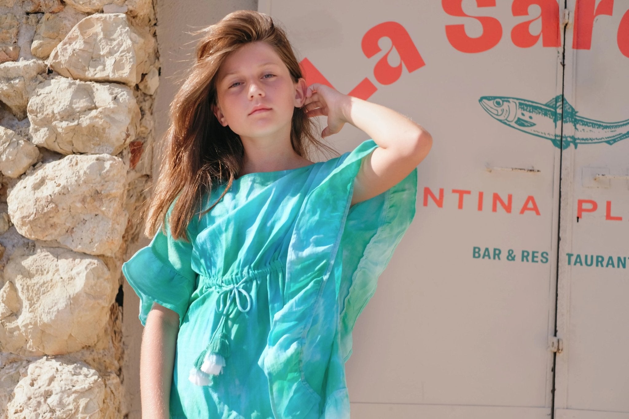 girl in turquoise beachwear standing outdoors by stone wall, summer fashion for kids