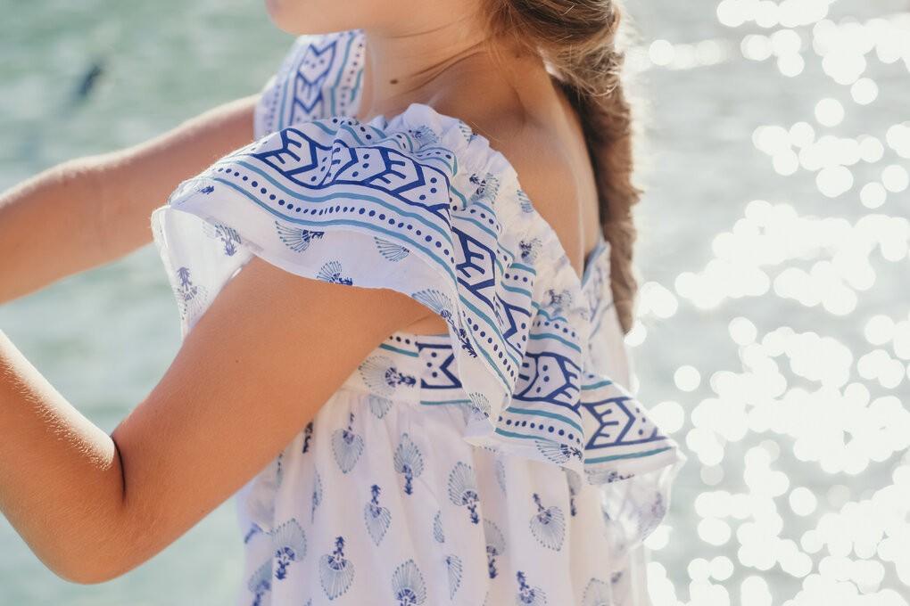 Girl in white and blue patterned summer dress with ruffled sleeves by the water