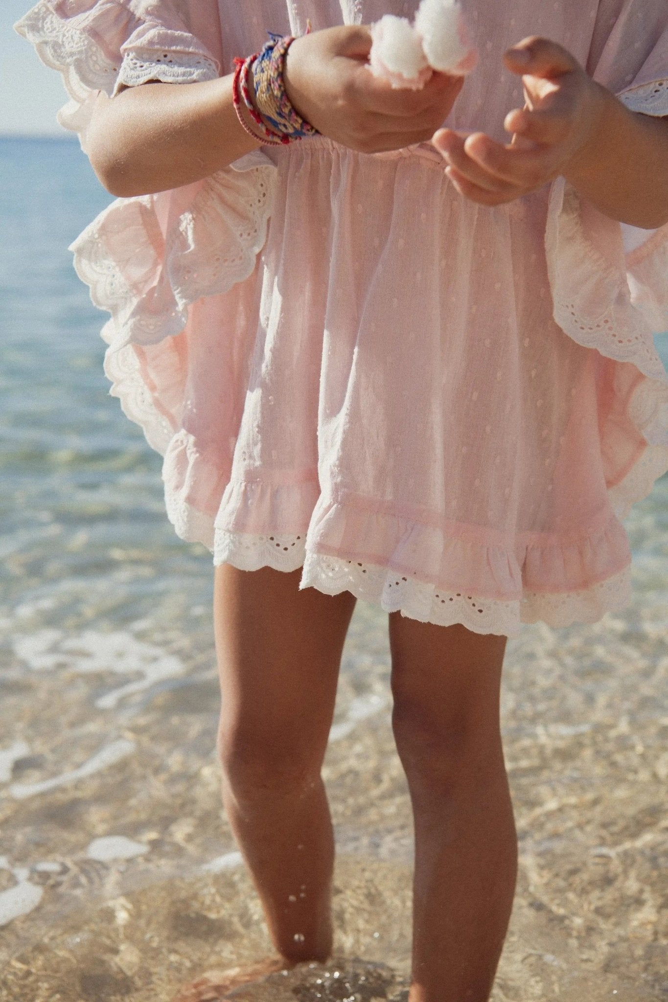 Girl in light pink beach caftan dress standing at the water's edge