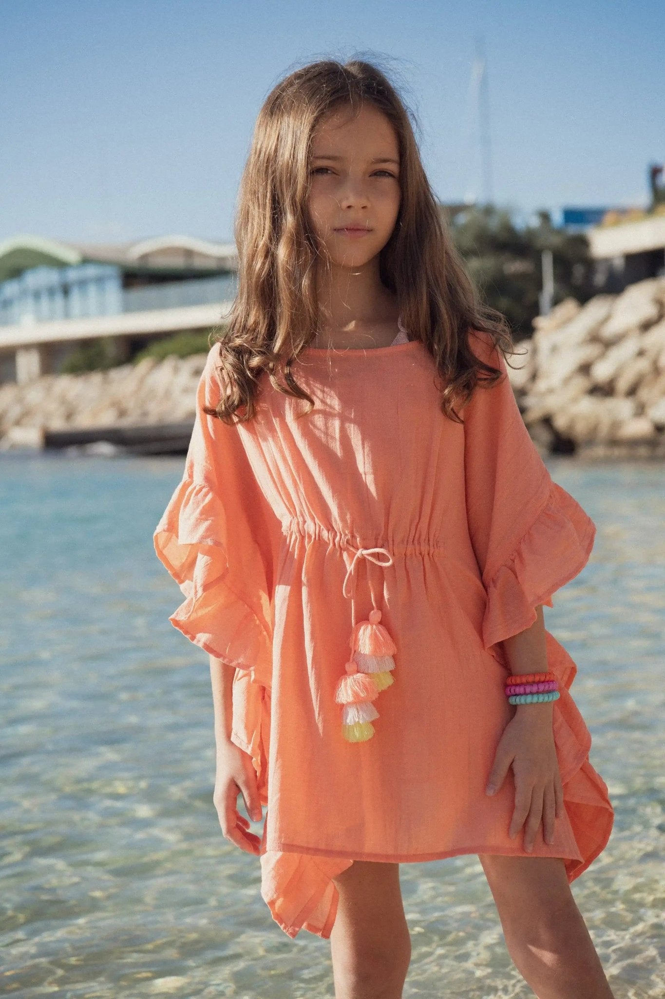 Girl in coral beach dress with ruffle sleeves standing by the seaside on a sunny day