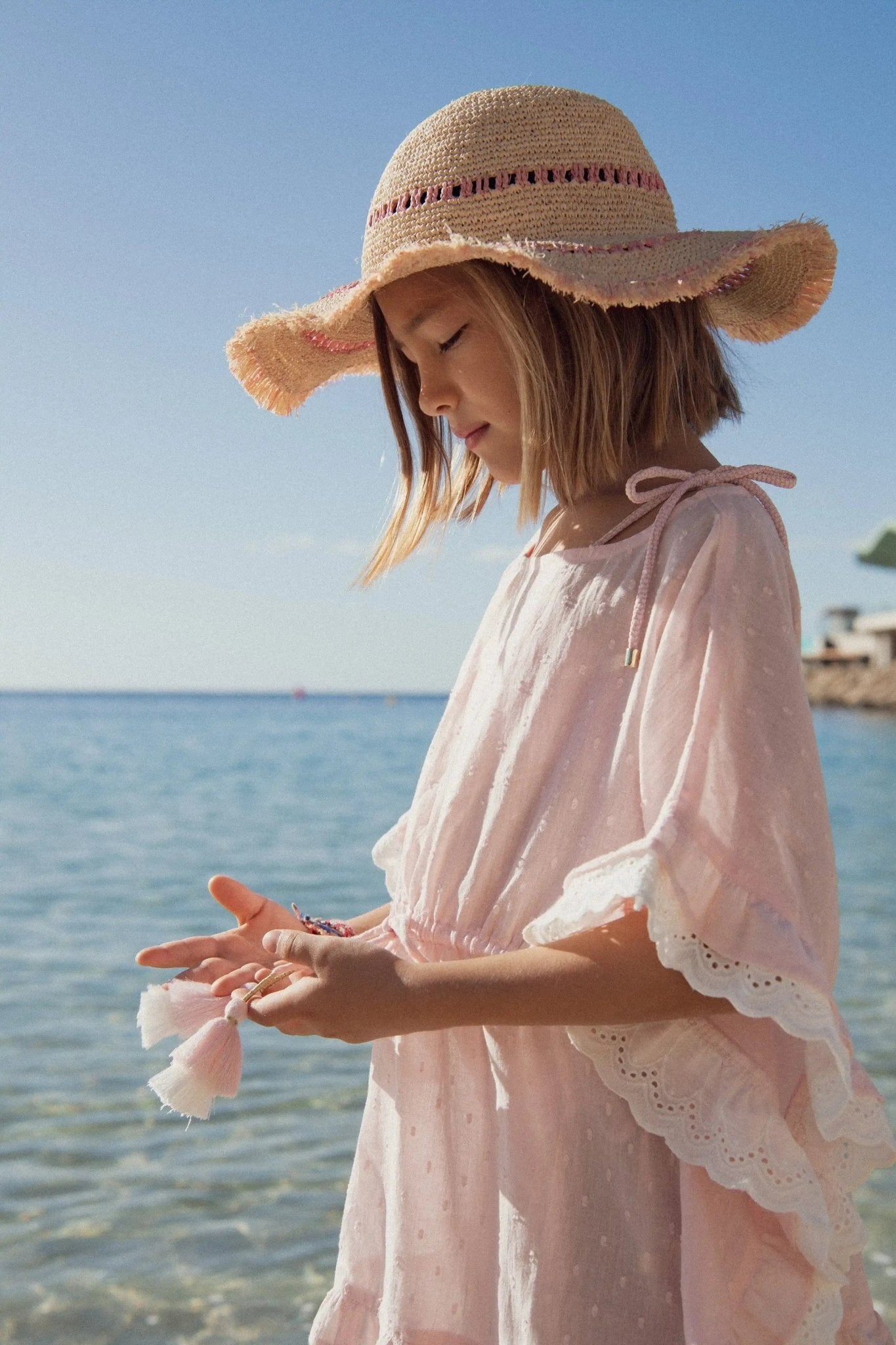 Girl in pink beach caftan and straw hat standing by the sea on a sunny day