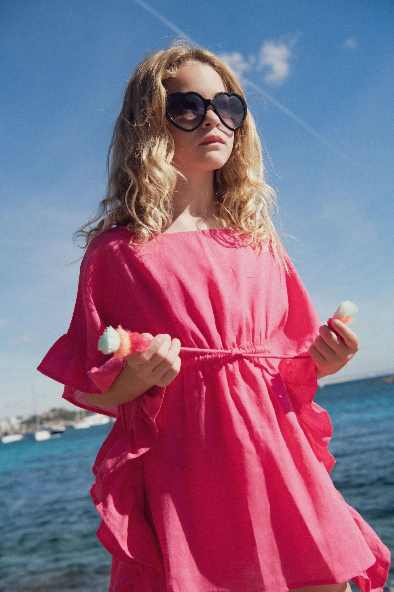 Girl in hot pink beach kaftan and heart sunglasses by the sea on a sunny day