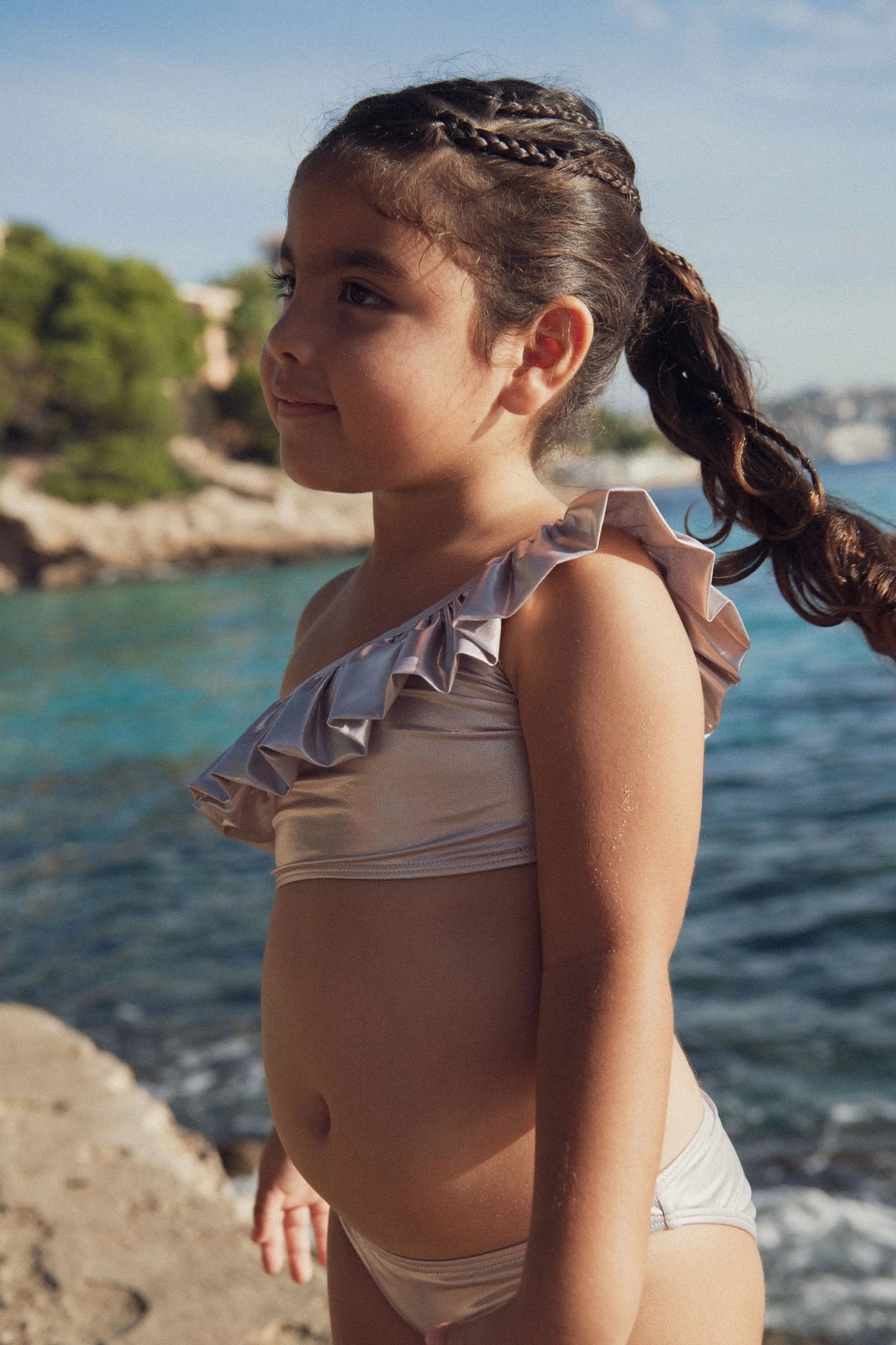 Girl wearing a one-shoulder ruffled swimsuit on a sunny beach by the sea