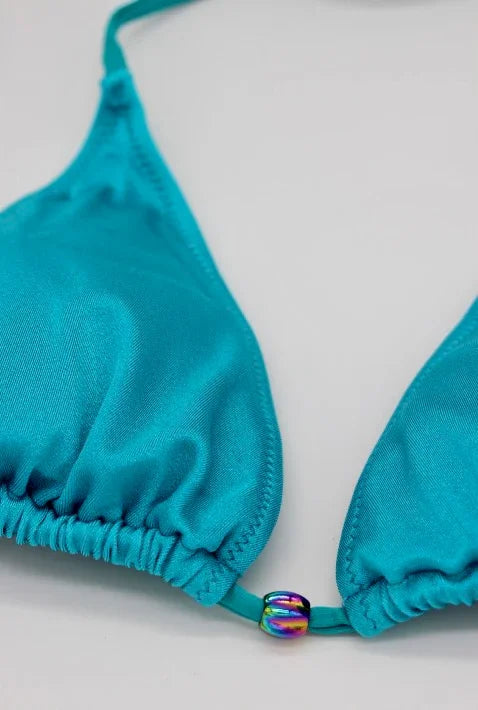 Close-up of turquoise triangle bikini top with iridescent bead detail on white background