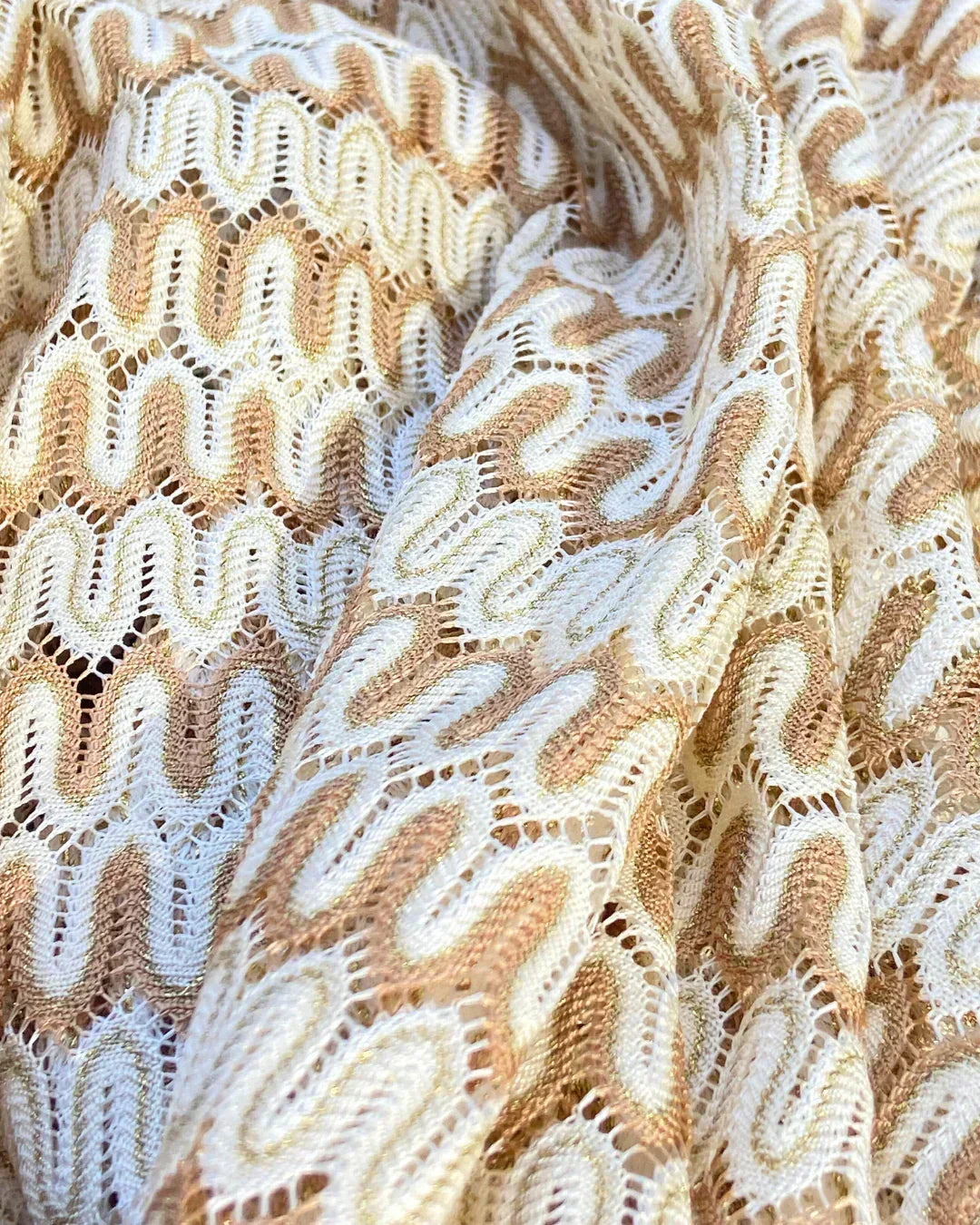 Close-up of white and gold crochet fabric with wavy pattern and open lace details