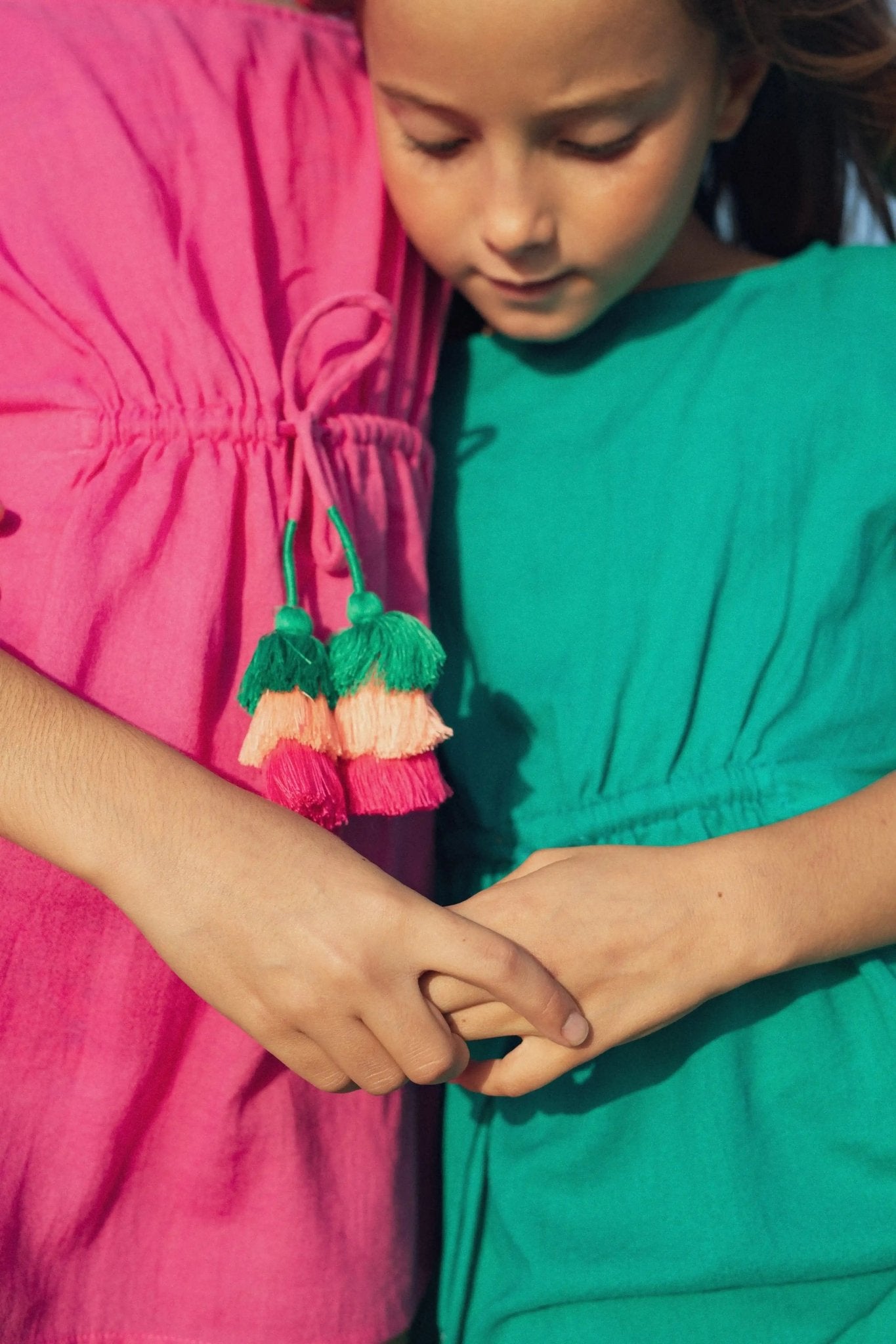 Two girls in bright green and fuchsia pompom caftans holding hands outdoors