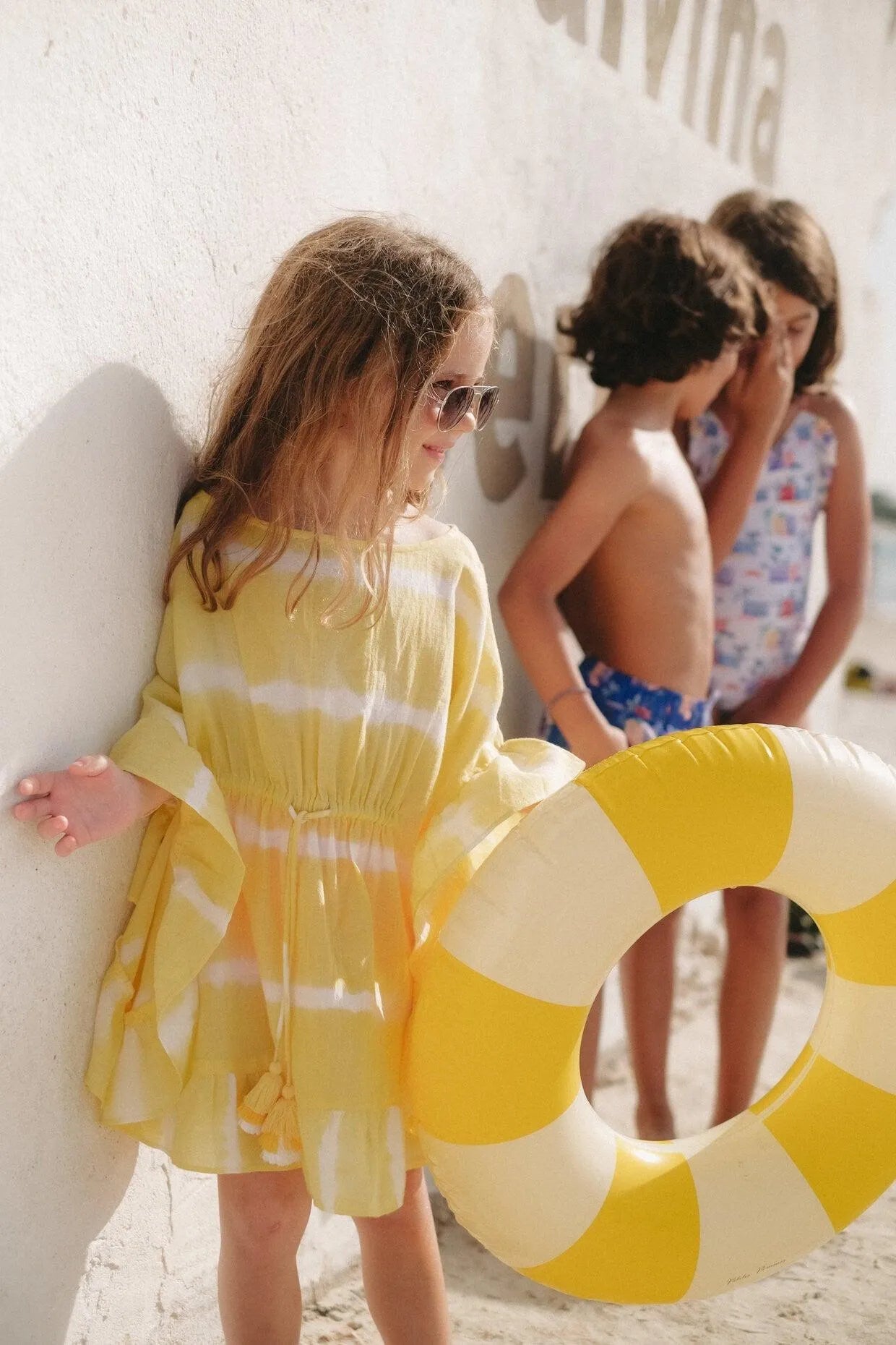 Girl wearing yellow tie-dye caftan and sunglasses holding yellow inflatable ring at sunny beach