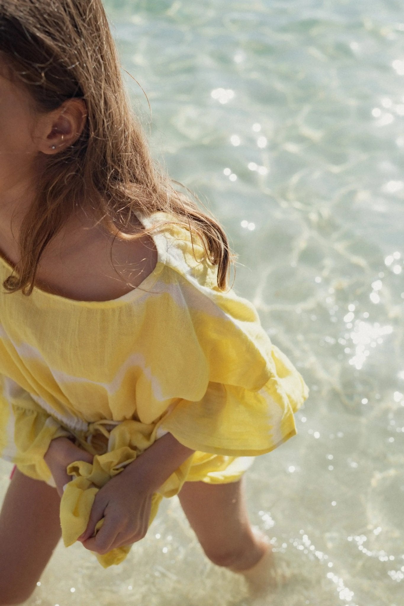 Girl in yellow tie-dye caftan standing in clear shallow beach water