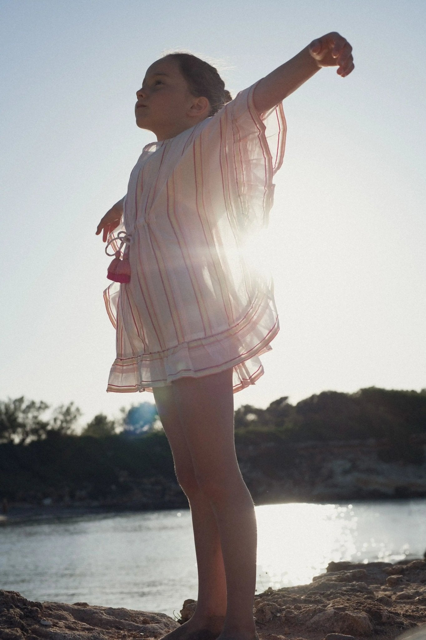 Girl wearing a pink striped caftan beach dress outdoors by the water on a sunny day