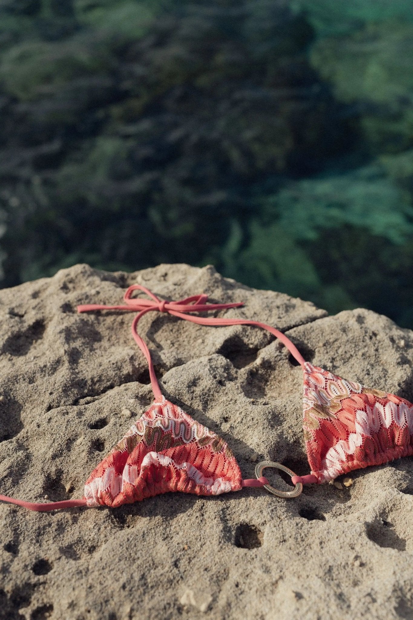Coral crochet bikini top with gold detail on rock by the sea