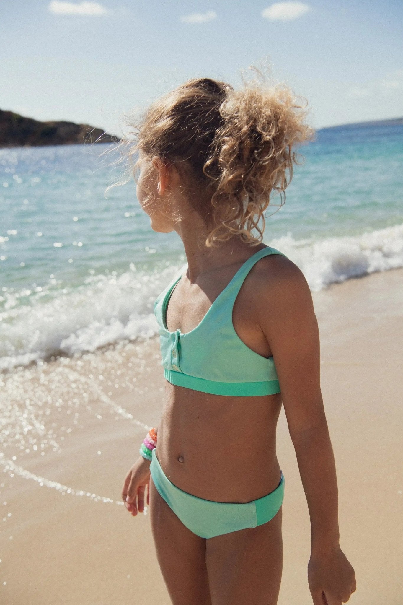 Girl in aqua two-piece UV swimwear standing on a sunny beach by the sea