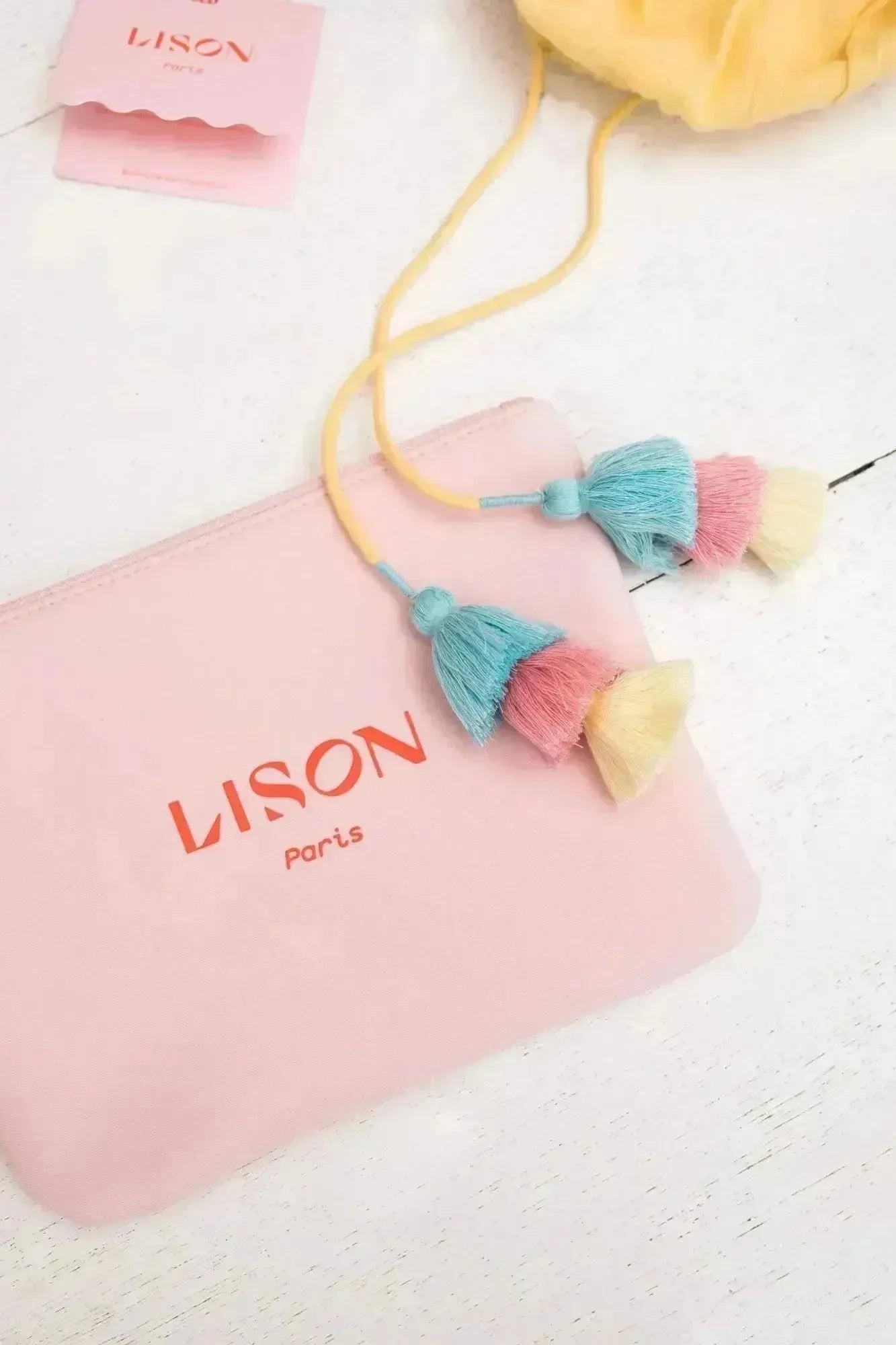 Pink Lison Paris pouch with colorful tassels on white wooden surface