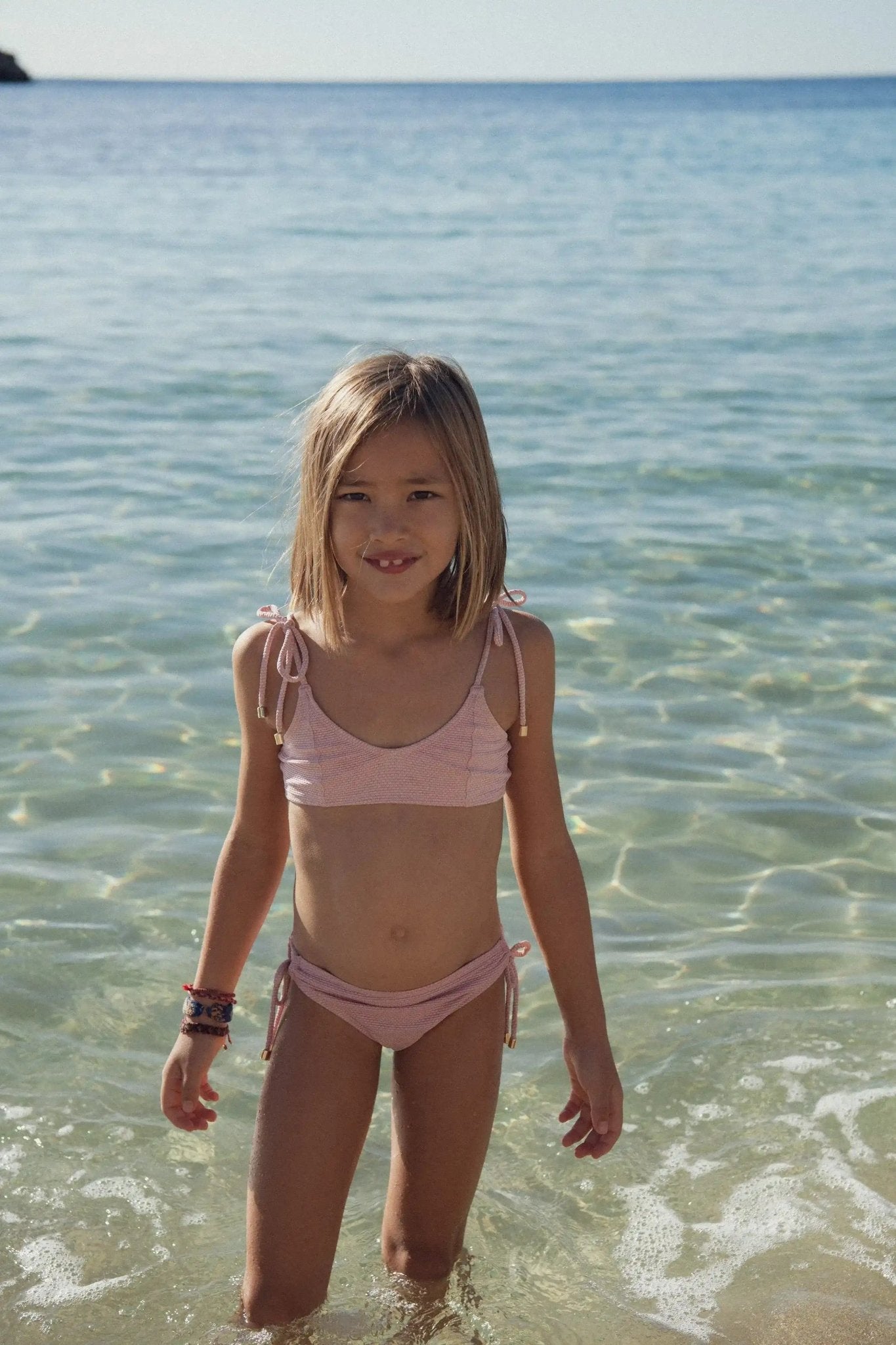 Girl wearing pale pink two-piece swimsuit standing in clear shallow sea water