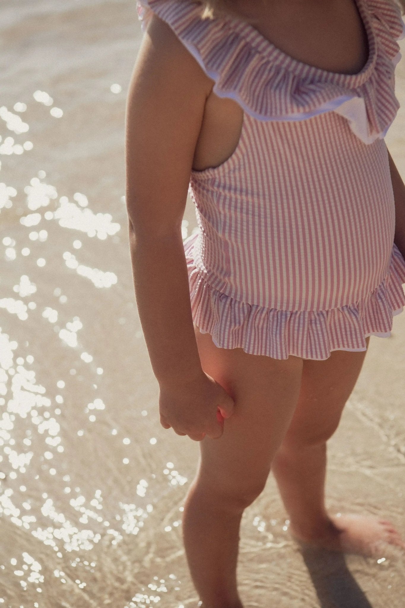 Girl wearing a lilac striped ruffled one-piece swimsuit standing on the beach