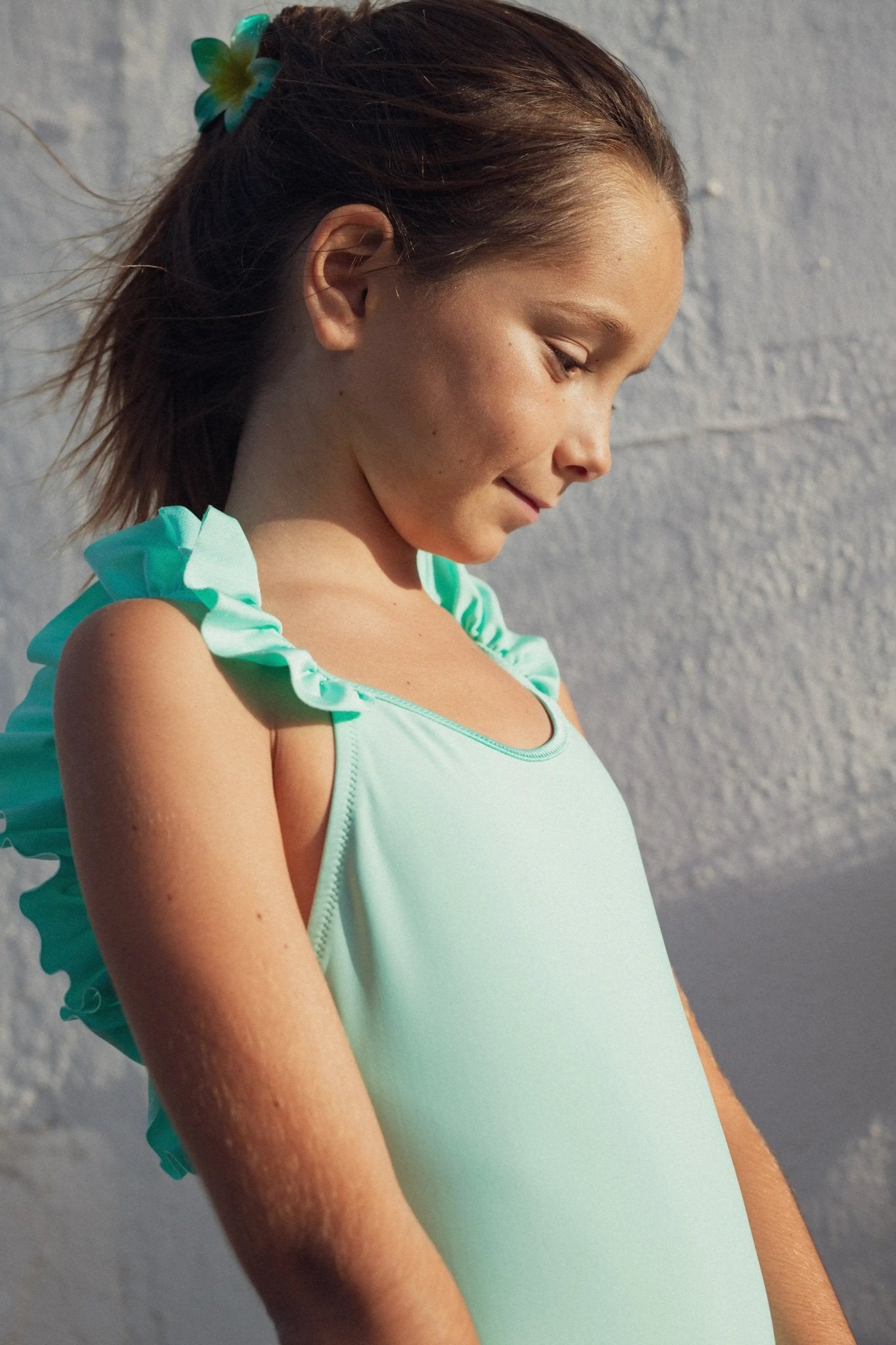 Girl wearing light blue one-piece ruffle swimsuit with UV protection in sunlight