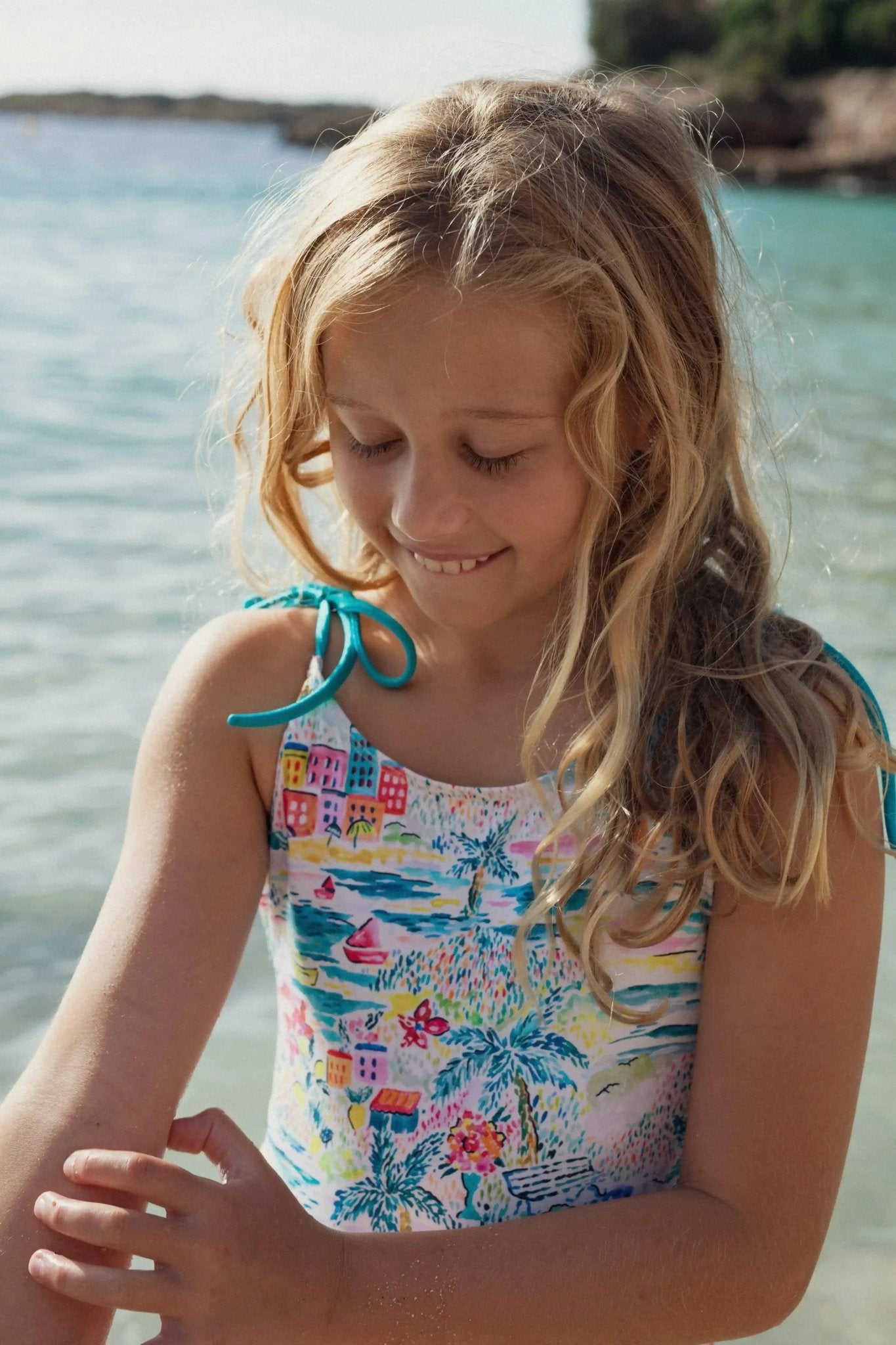 Young girl in a colorful one-piece swimsuit with tropical print standing by the sea