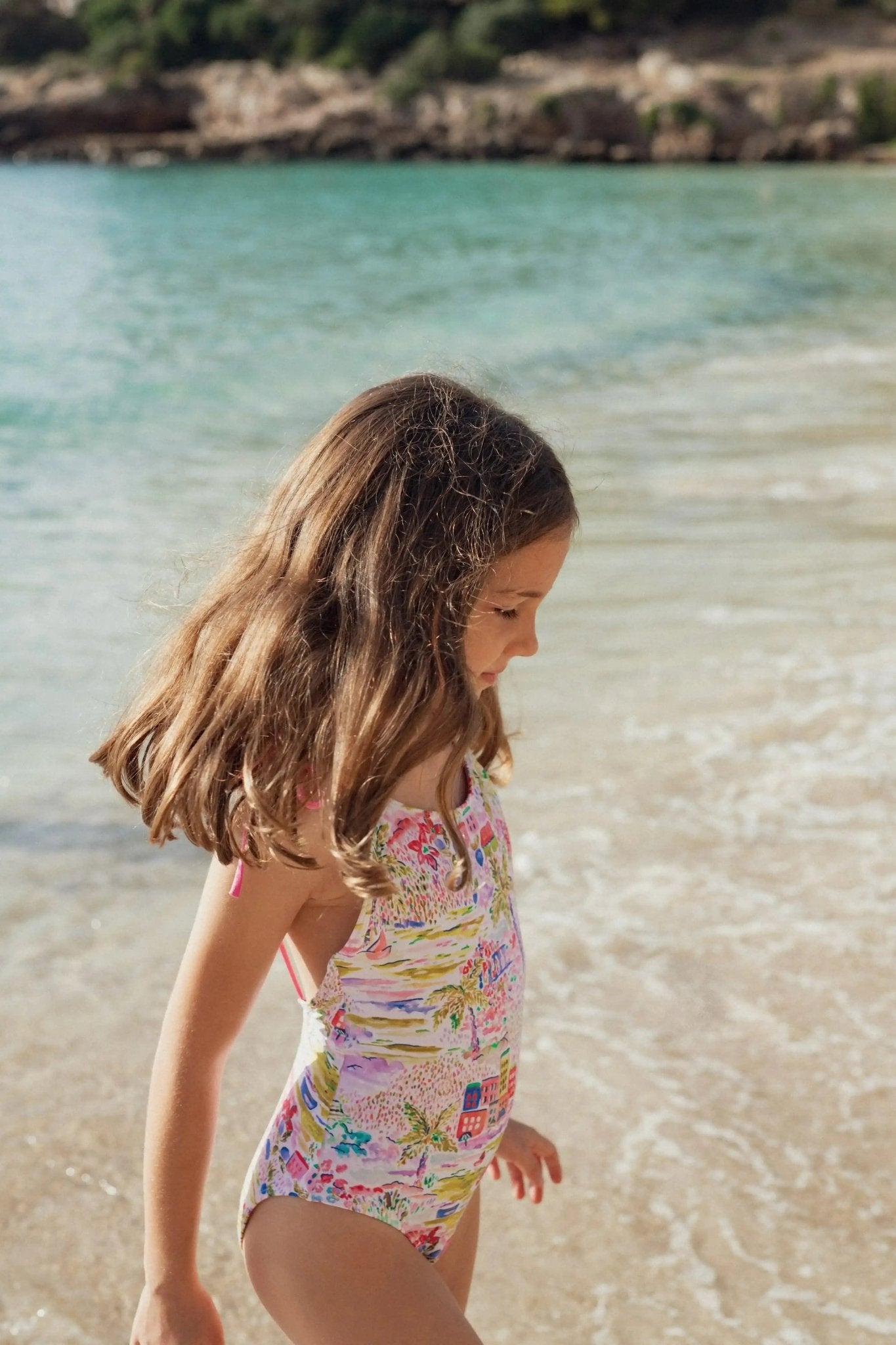 Girl in colorful one-piece swimsuit walking on the beach by the sea