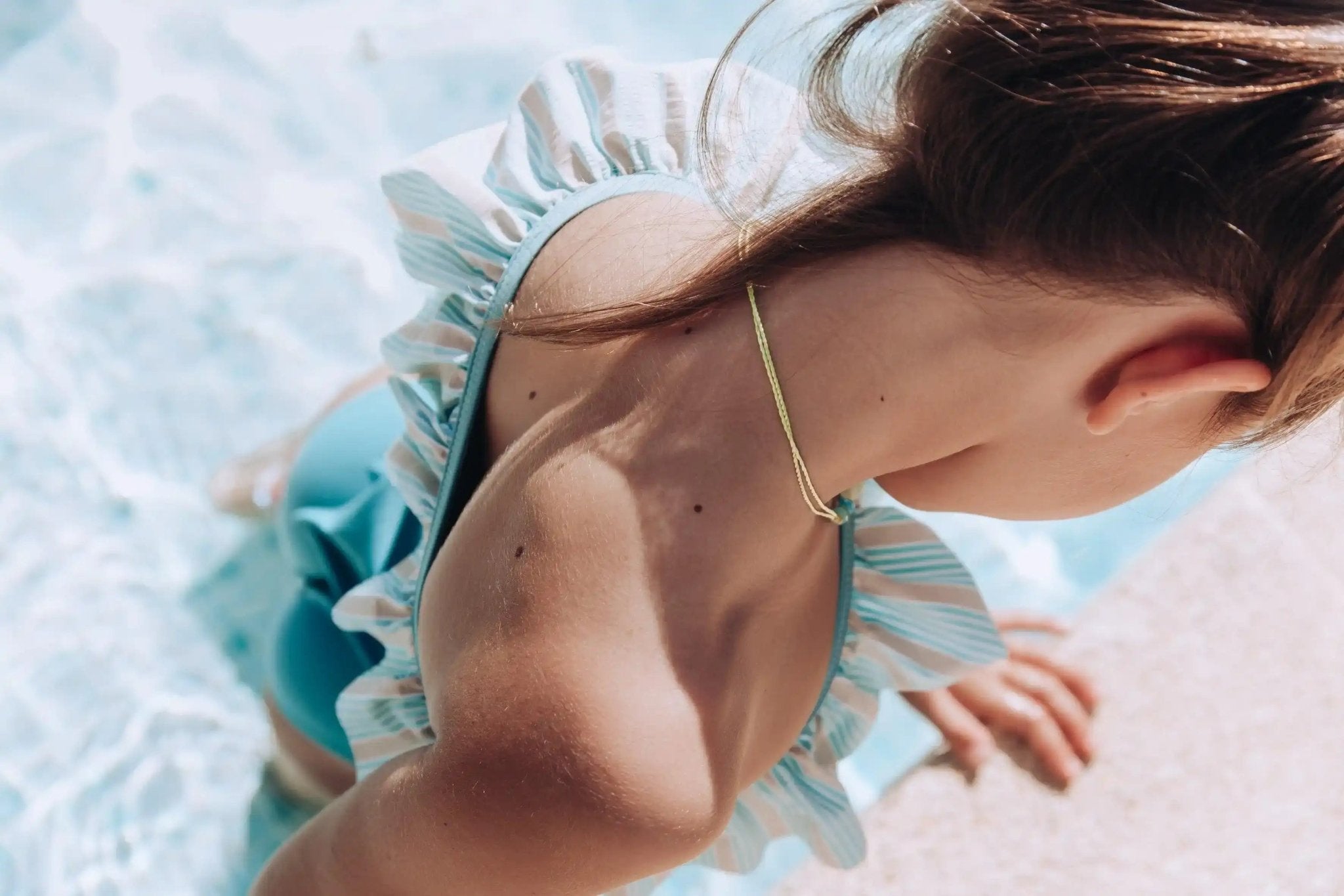 Girl in blue and white striped ruffle one-piece swimsuit by the pool