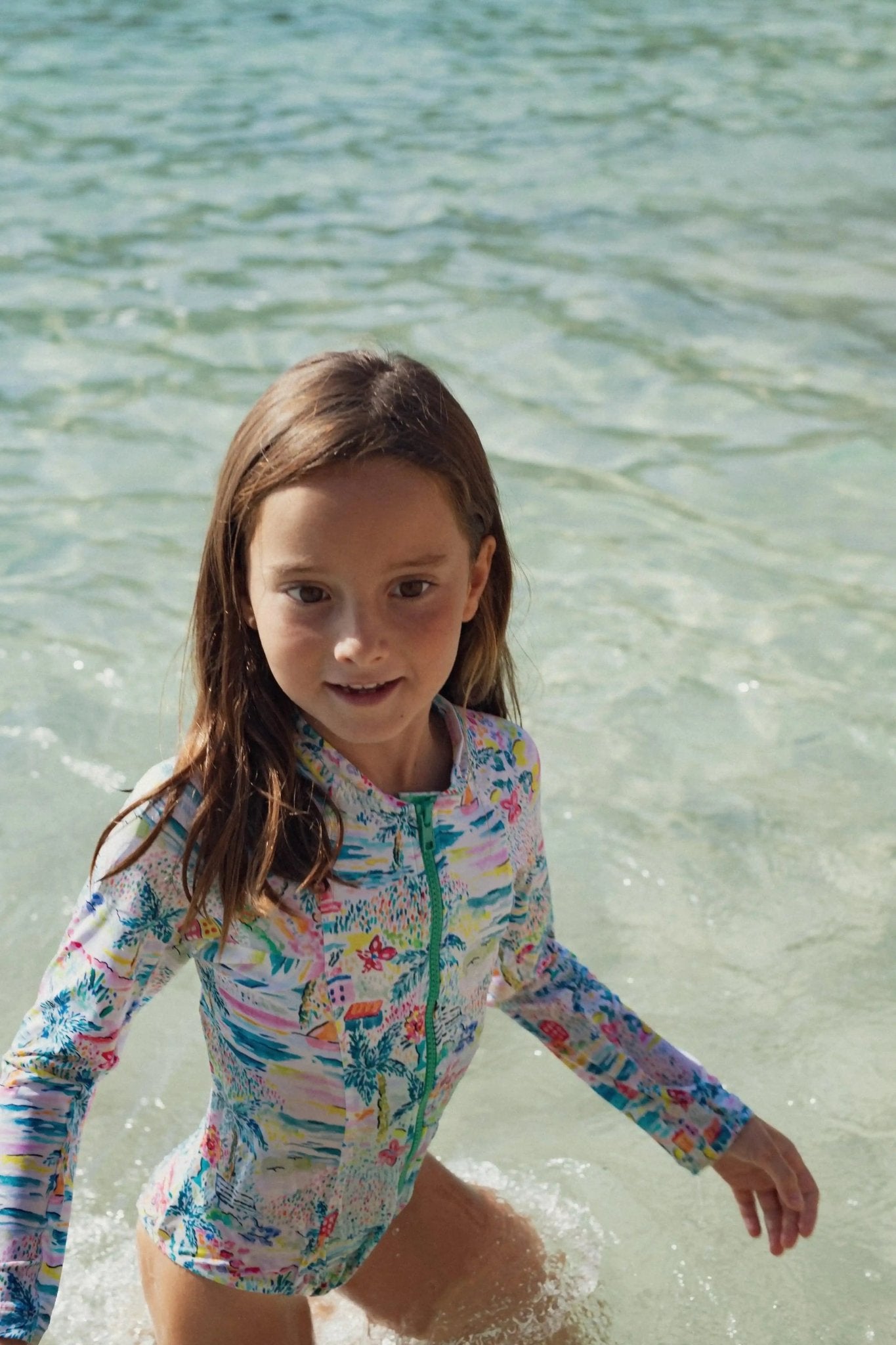 Girl in a colorful long sleeve one-piece swimsuit playing in clear shallow water
